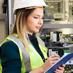 woman in safety vest and hard hat writing on clipboard