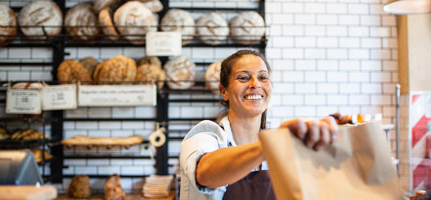 Bakery owner hands baked goods to customer across counter