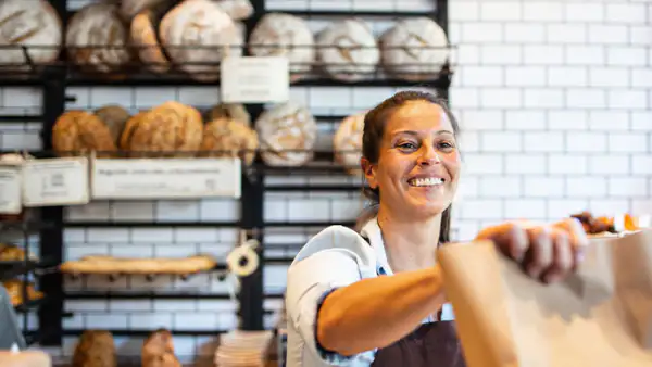 Bakery owner hands baked goods to customer across counter