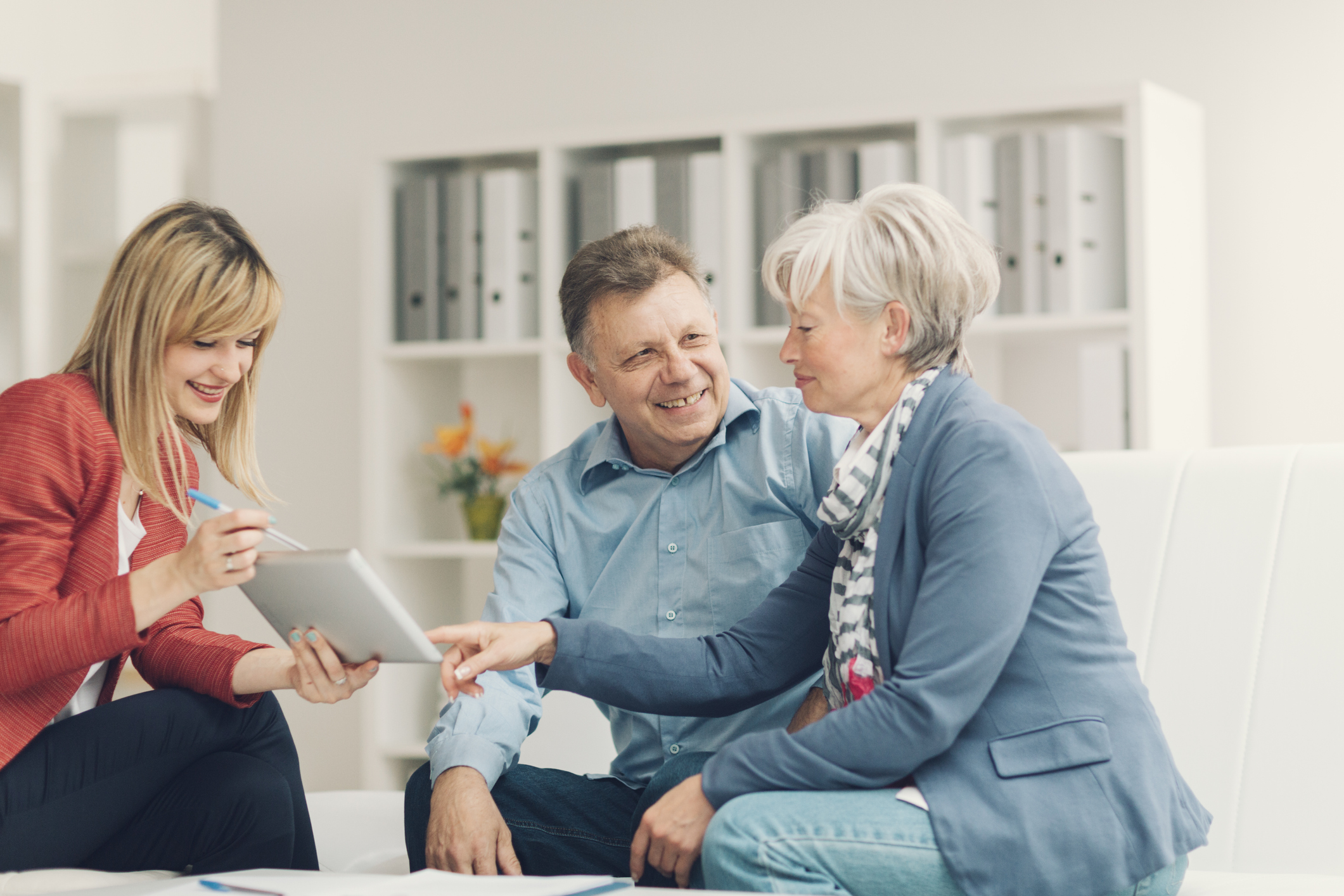 Mature Woman pointing with index finger to digital tablet and asking financial advisor for explanation.