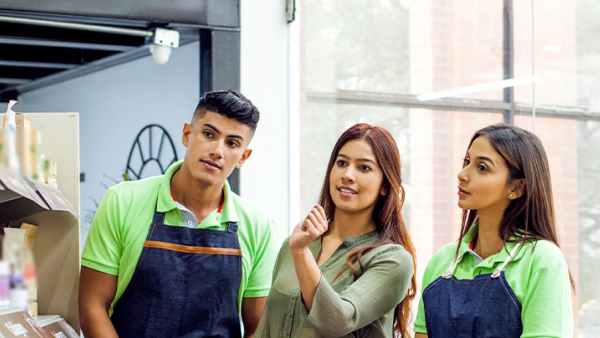 Three good looking people in aprons looking at something on shelves