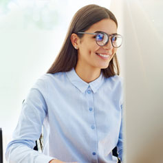 Woman with glasses smiling staring at a computer screen
