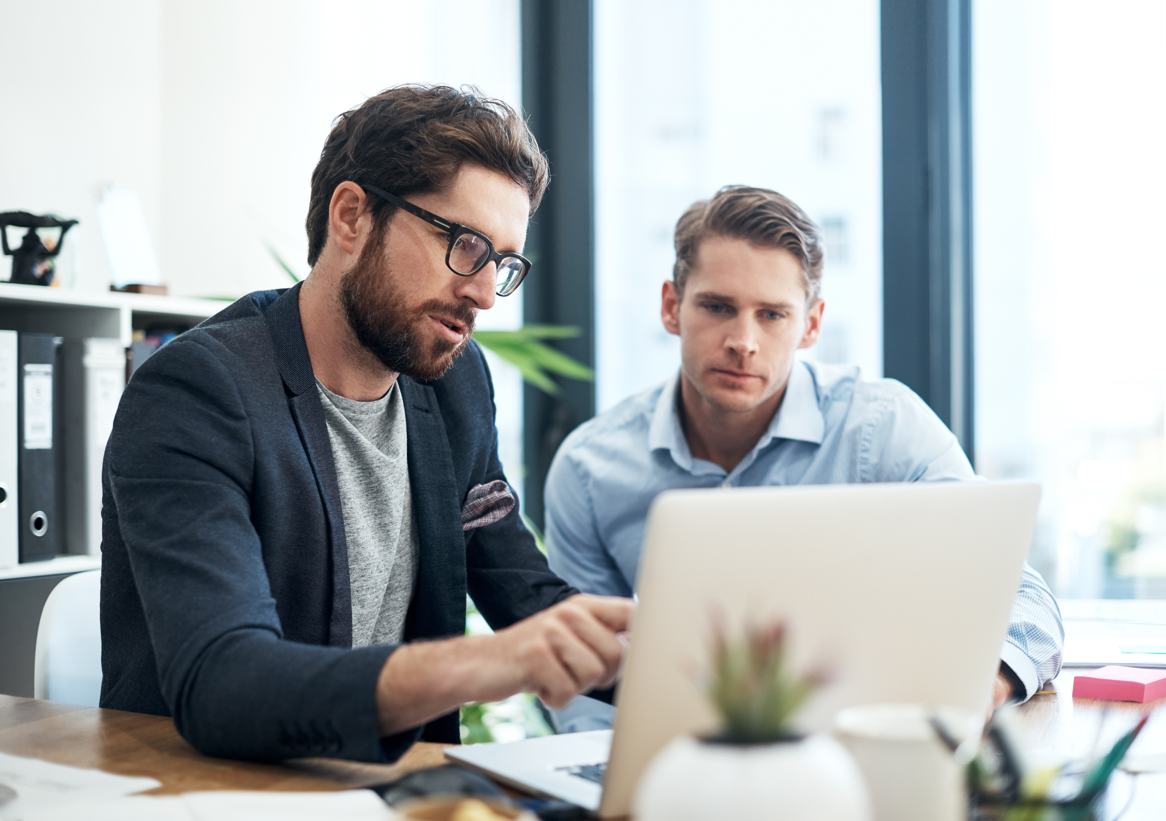 Two HR employees sit at a desk and look at a laptop.